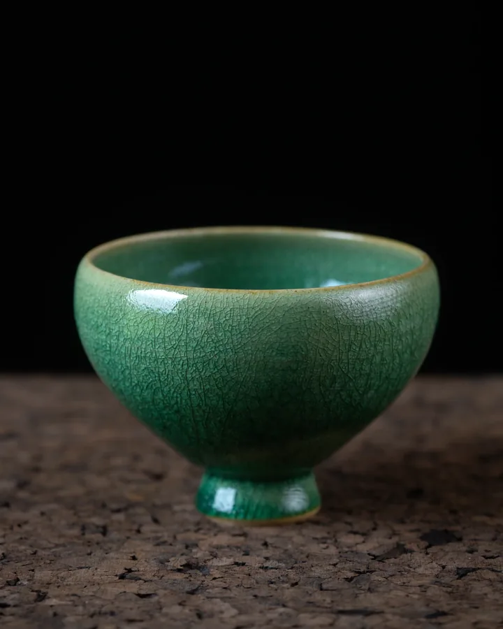 Deep green crackle bowl: a deep bowl on a pedestal foot in teal-green crackle glaze, against black